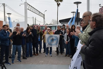 Varias personas aplauden en una plaza mientras un hombre sostiene una bandera blanca con un emblema circular azul
