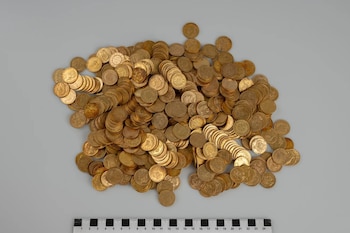 Un montón de monedas doradas apiladas sobre una superficie gris junto a una regla numerada en el borde inferior