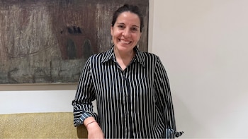 Una mujer sonriendo, vestida con camisa de rayas verticales blancas y negras, posa frente a una pared clara con un cuadro abstracto