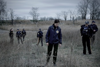 Siete personas con uniformes de policía y gorras en un campo con hierba seca y arbustos, y árboles sin hojas bajo un cielo gris