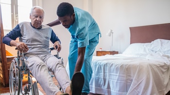 Un auxiliar de enfermería ayuda a un anciano en silla de ruedas.