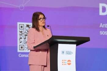 Una mujer con gafas y traje rosa habla desde un atril con los logotipos de la Secretaría de Planificación de la Presidencia y el UNFPA