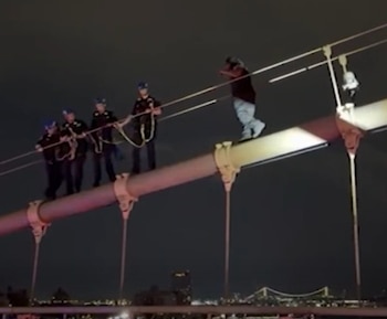 Cuatro agentes de policía con cascos avanzan sobre una estructura metálica inclinada hacia un hombre durante la noche