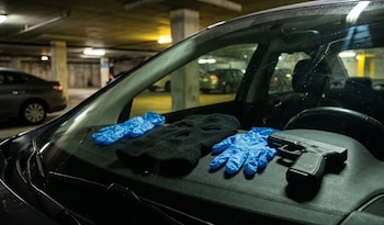 Una máscara de esquí negra, guantes de látex azules y una pistola semiautomática negra se ven sobre el tablero de un coche en un estacionamiento