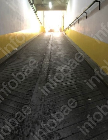 Vista frontal de una rampa oscura de hormigón en un túnel con paredes blancas y una franja amarilla, que conduce a una salida muy luminosa al exterior