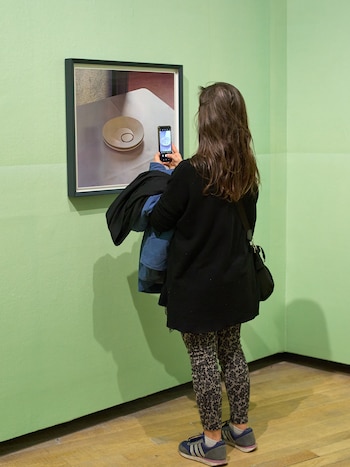 Una mujer de espaldas fotografía con su teléfono un cuadro colgado en una pared verde