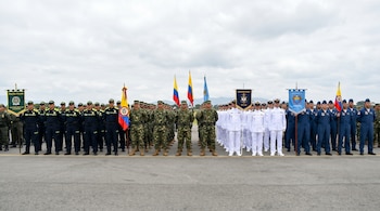 Vista frontal de diferentes ramas de las fuerzas militares y policía de Colombia, formadas en una pista de asfalto con banderas y estandartes.