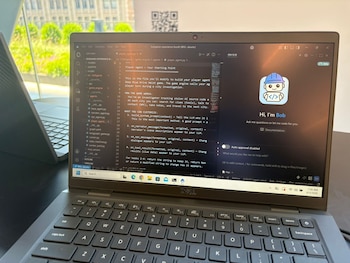 Una laptop Dell negra abierta muestra una pantalla con código de programación y la interfaz del asistente de IA IBM BOB. Se ve parte del teclado y un fondo de ventana