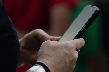 Manos de una persona que sostienen y operan un teléfono inteligente con la pantalla iluminada sobre un fondo desenfocado