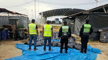 Cuatro agentes, dos con chalecos de SUNAT y dos de la Policía, observan una gran cantidad de bolsas negras llenas sobre una lona azul en un área industrial