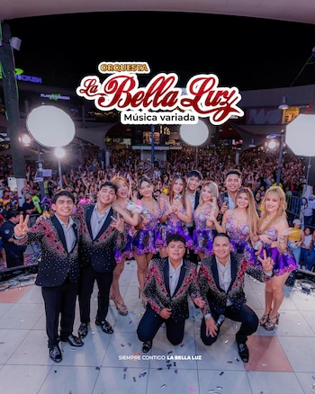 Grupo musical de once integrantes en un escenario. Hombres con trajes negros brillantes, mujeres con vestidos cortos morados. Público numeroso detrás en la noche