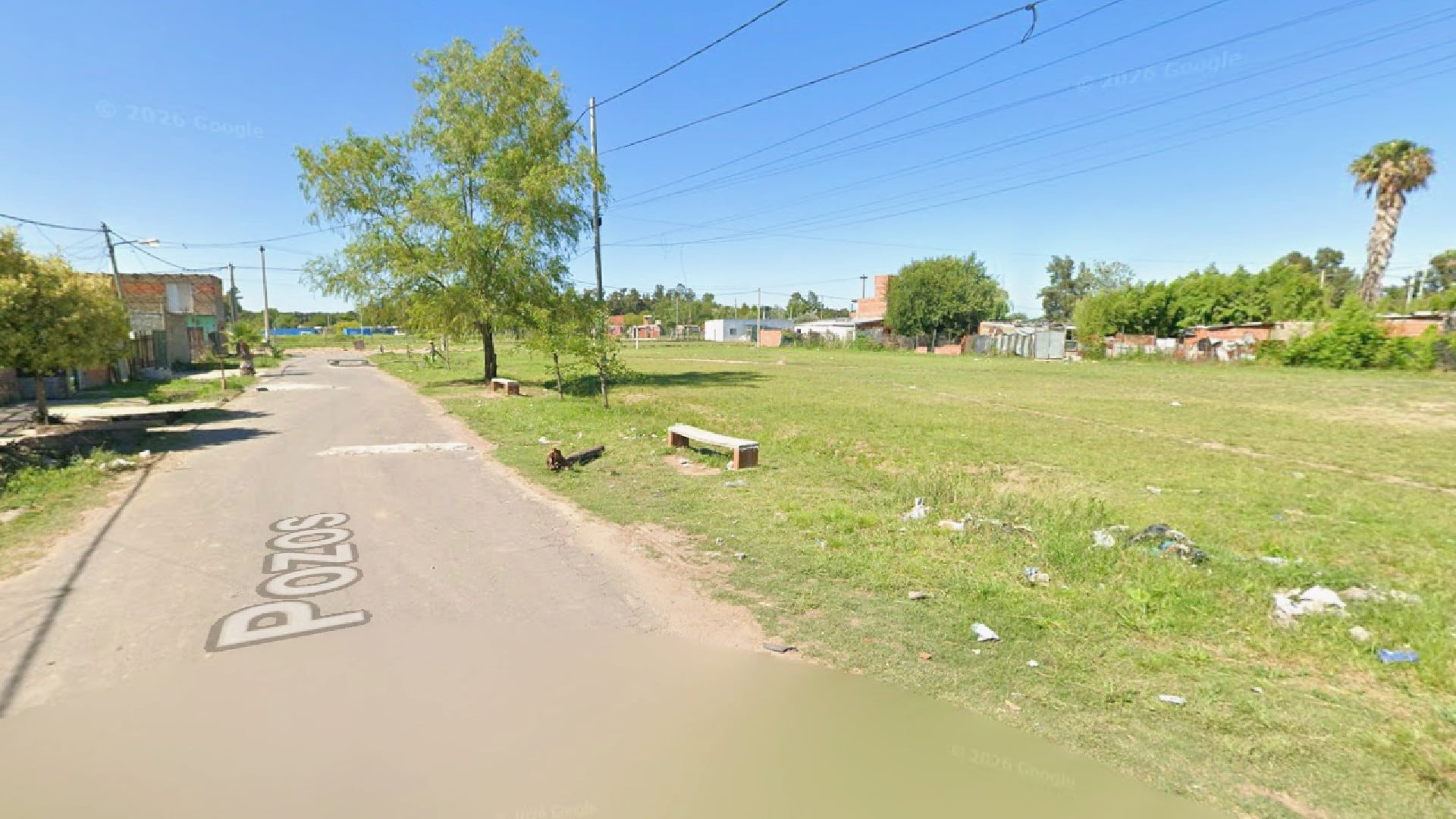 La calle Pozos en Rosario, el lugar preciso donde una mujer fue asesinada a quemarropa, se presenta con un terreno baldío adyacente y modestas construcciones a lo lejos.
