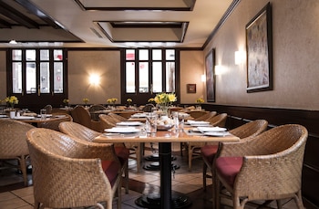 Interior de Le Cafe Restaurante con mesas de madera preparadas, sillas de mimbre con cojines rojos, jarrones con flores amarillas y ventanas al fondo