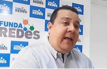 Primer plano de un hombre con camisa de rayas, hablando ante un fondo azul y blanco con el logo de Funda Redes repetido