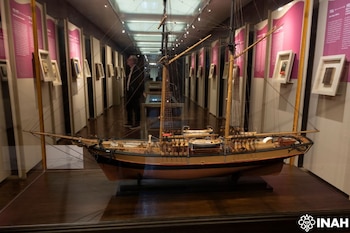Modelo de barco velero en vitrina de cristal. Mástiles, aparejos, botes. Pasillo de museo, paneles informativos, marcos, hombre. Logo INAH
