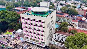 Vista aérea de un edificio blanco de seis pisos con detalles rosados, personas congregadas en la calle y una terraza cubierta en la azotea