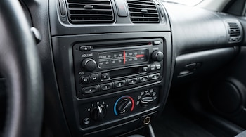 Radio analógica de un automóvil con perillas de volumen y sintonización, dial de frecuencias, rejillas de ventilación y controles de aire.