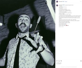 Fotografía en blanco y negro de un hombre barbudo con camisa estampada y corbata oscura, abriendo la boca y mirando hacia arriba, con la mano izquierda levantada
