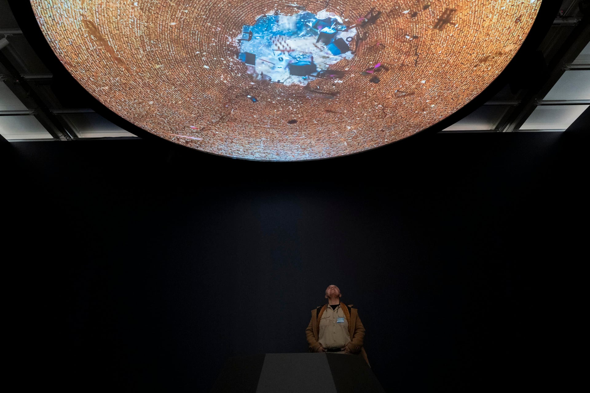 Un visitante mira hacia arriba una gran proyección circular de arte digital inmersivo, en una sala oscura durante la Bienal 2026 del Museo Whitney de Nueva York.