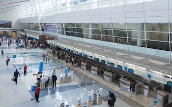 Vista panorámica de una moderna terminal de aeropuerto con techos altos y ventanales. Se ven pasajeros, mostradores de check-in, quioscos y equipaje