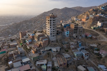 Casas de ladrillo y cemento agrupadas en la ladera de un cerro alrededor de una edificación alta sin terminar.