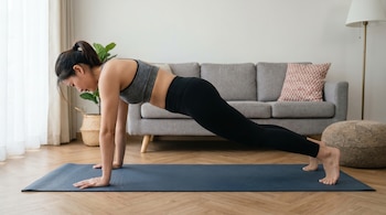 Una mujer realiza una plancha abdominal en una esterilla azul. Sus caderas están caídas, indicando una postura incorrecta en un entorno hogareño.