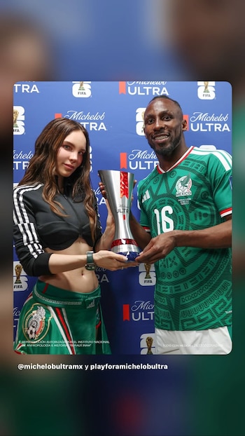 Una mujer y un hombre sujetan un trofeo plateado y rojo. El hombre viste una playera verde de fútbol con el número 16. Fondo azul con logotipos