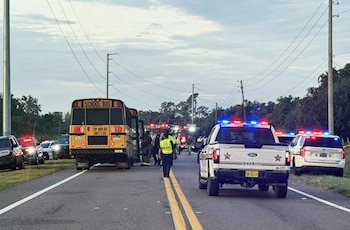 Un autobús escolar amarillo y varios vehículos de la policía con luces de emergencia encendidas en una carretera
