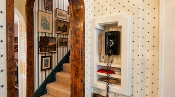 Teléfono negro de pared en nicho blanco empotrado. Pared con papel pintado de estrellas. A la izquierda, una escalera con alfombra de sisal y cuadros en pared a rayas.