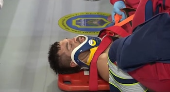 Hombre acostado en una camilla de rescate roja, con collarín cervical azul y blanco, siendo atendido por personal médico con guantes