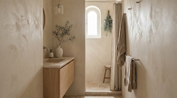 Interior de un baño moderno en tonos neutros con lavabo de madera, espejo, ventana arqueada, ducha con cortina y toallas colgadas.