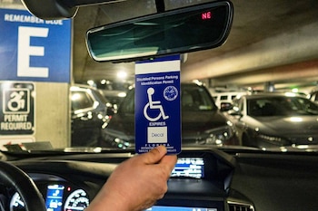 Mano de persona sostiene un permiso azul de estacionamiento para personas con discapacidad dentro de un coche, en un estacionamiento subterráneo