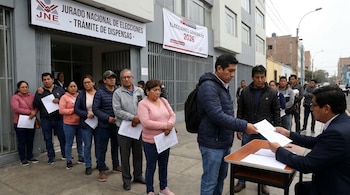 Una fila de ciudadanos espera frente a un edificio del JNE con cartel "Trámite de Dispensas". Un hombre entrega documentos a un oficial sentado en una mesa.