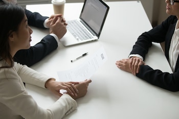 Una mesa blanca alrededor de la que se sientan tres personas: dos mujeres y un hombre. Una de las mujeres mira el curriculum