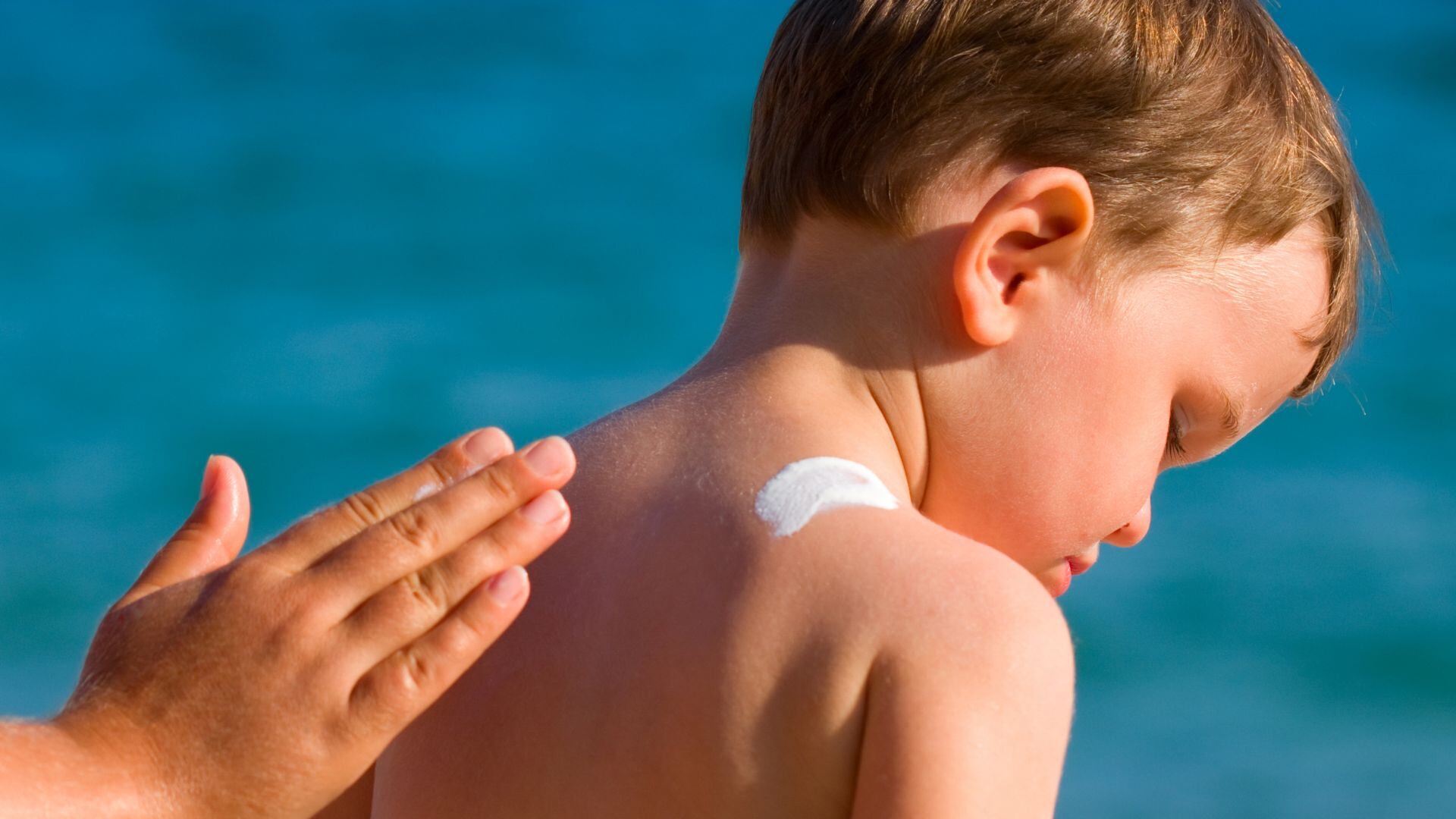 Una madre aplica crema solar en la espalda a su hijo (Canva)