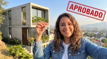 Mujer latina sonriente sostiene llaves frente a una casa moderna de concreto y el horizonte de la Ciudad de México. Un sello rojo superpuesto dice "APROBADO".