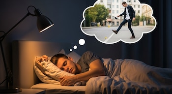 Un hombre duerme en una cama con luz cálida de una lámpara de noche. Sobre él, una burbuja muestra su sueño de resbalar con una cáscara de banana en la calle.