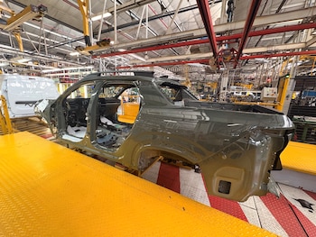 Carrocería verde sin puertas ni ruedas sobre una plataforma de transporte en el interior de una planta industrial