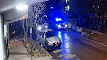 Un vehículo policial con luces azules encendidas y un automóvil gris estacionado en una calle pavimentada durante la noche.