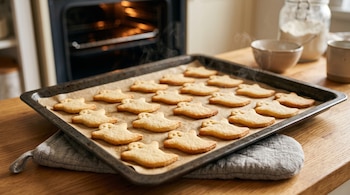 Galletas doradas con forma de fantasma sobre papel vegetal en una bandeja de horno encima de un paño en un mostrador de madera.