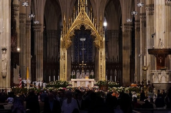 Vista interior de una gran Catedral con un altar central adornado con flores blancas, un retablo dorado y una congregación de personas