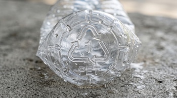 Base de una botella plástica con gotas de agua y el símbolo de reciclaje número uno PET en relieve, sobre una superficie de hormigón.