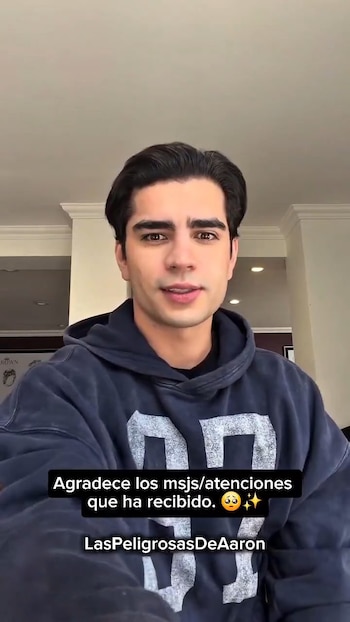 Hombre joven con sudadera azul oscuro sonríe a la cámara. Texto superpuesto: "Agradece los msjs/atenciones que ha recibido." y "LasPeligrosasDeAaron"