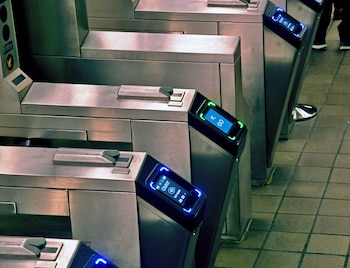 Varios torniquetes metálicos con pantallas digitales iluminadas en azul y verde. Algunas muestran el logo OMNY, otras la palabra GO