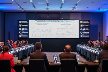 Personas en una sala de conferencias. Pantalla grande exhibe gráficos sobre comercio global, importaciones, exportaciones y logos institucionales de Centroamérica