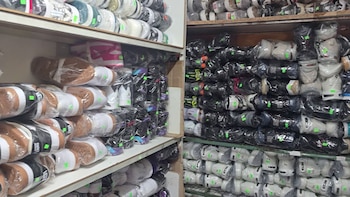 Vista detallada de estanterías abarrotadas con múltiples pares de zapatillas de deporte, cada una envuelta en plástico transparente con etiquetas verdes