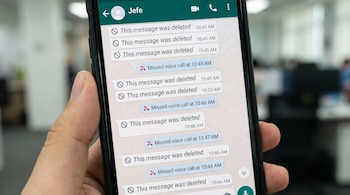 Primer plano de una mano sosteniendo un smartphone que muestra un chat de WhatsApp con el contacto "Jefe", repleto de mensajes eliminados y llamadas perdidas.