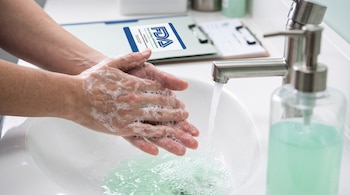 Manos con espuma de jabón bajo un grifo sobre un lavabo blanco, junto a un dispensador de jabón y una carpeta con la insignia de la FDA.