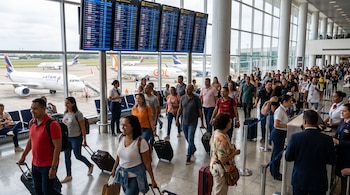 Terminal de aeropuerto internacional con pasajeros, equipaje, paneles electrónicos, aviones y personal.