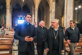 Varios hombres vestidos con alzacuellos clericales caminan por una iglesia entre bancos de madera y columnas de piedra
